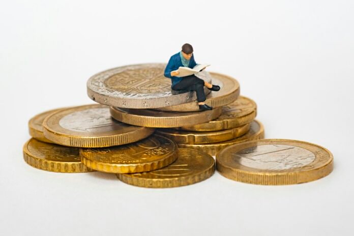 Miniature figure reading financial news while sitting on a stack of coins, representing investing and treasury bills